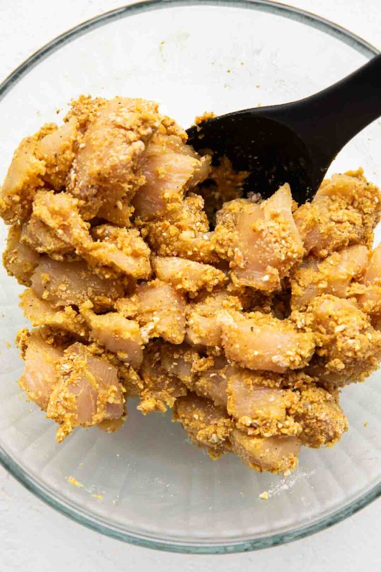 Honey mustard chicken tossed in breading in a bowl.