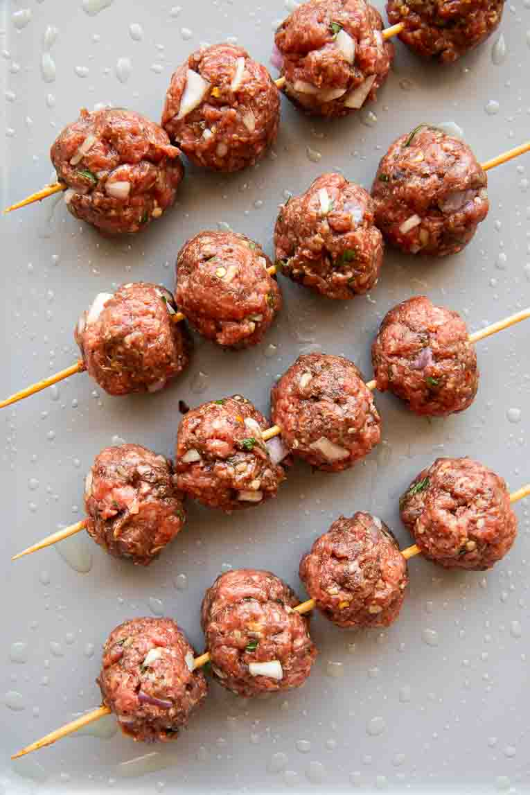Raw Lebanese meatballs on skewers over a baking sheet.