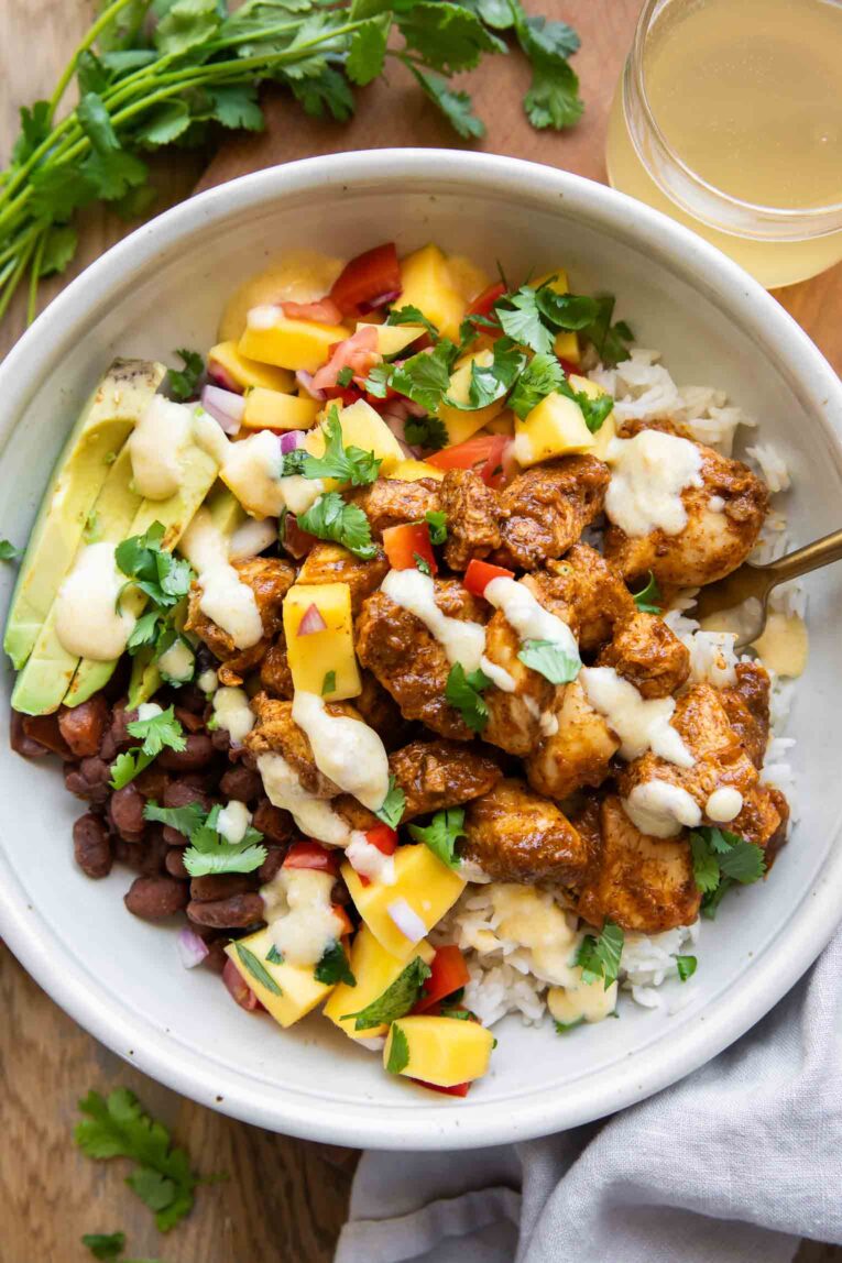 Mango Habanero Chicken in a bowl with avocado, beans, rice, and sauce.