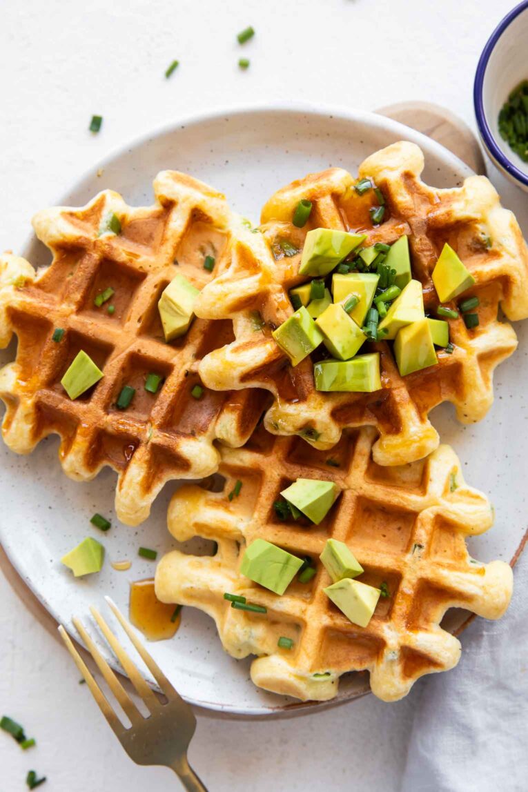 Savory waffles on a plate with hot honey and avocado.