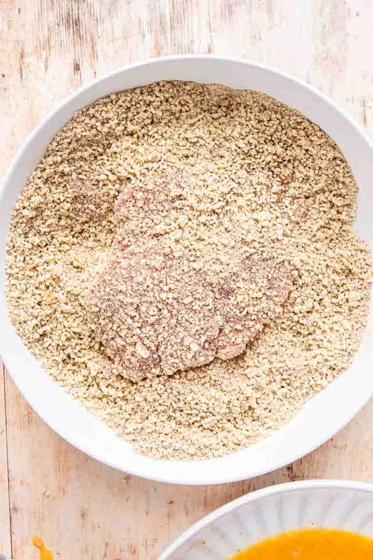 Chicken being breaded in a bowl.