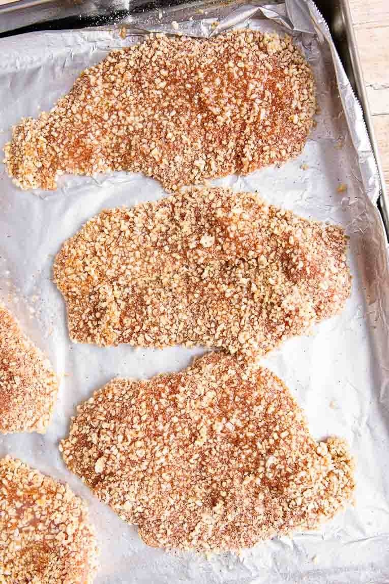 Breaded chicken slices on a baking sheet.