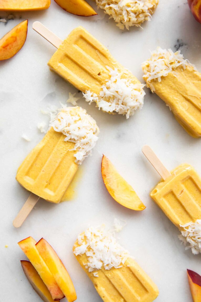 Coconut Turmeric Peach Popsicles on a marble countertop.