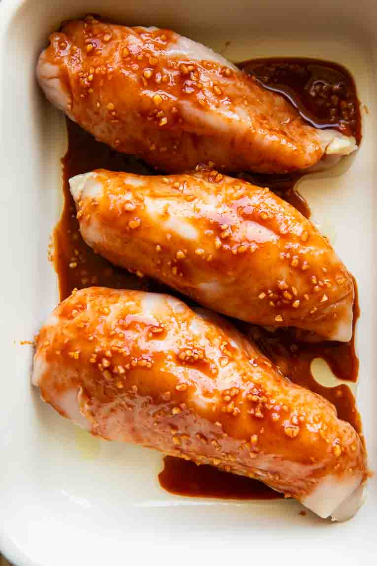 Chicken topped with sriracha in a baking dish.