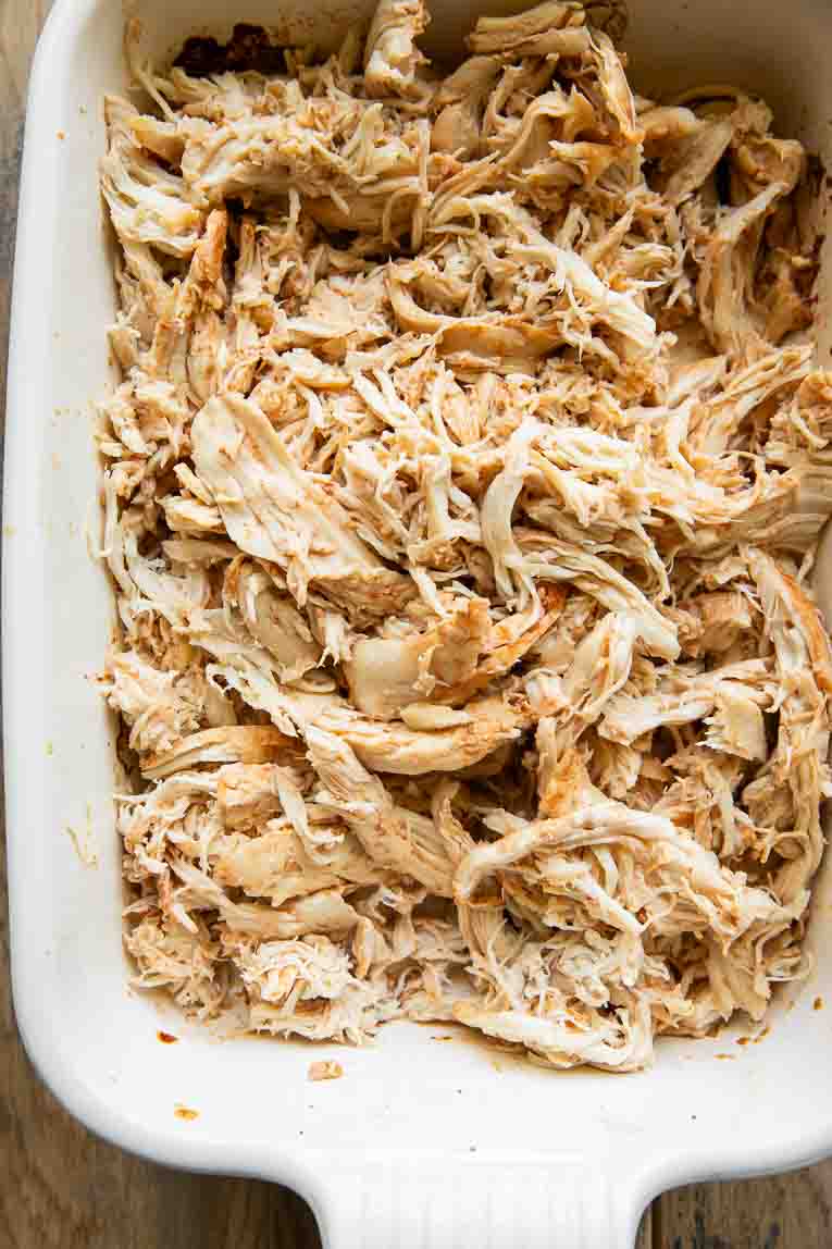 Baked sriracha chicken being shredded in a baking dish.