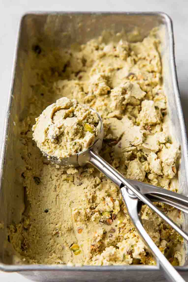 Pistachio ice cream in a loaf pan with an ice cream scoop.
