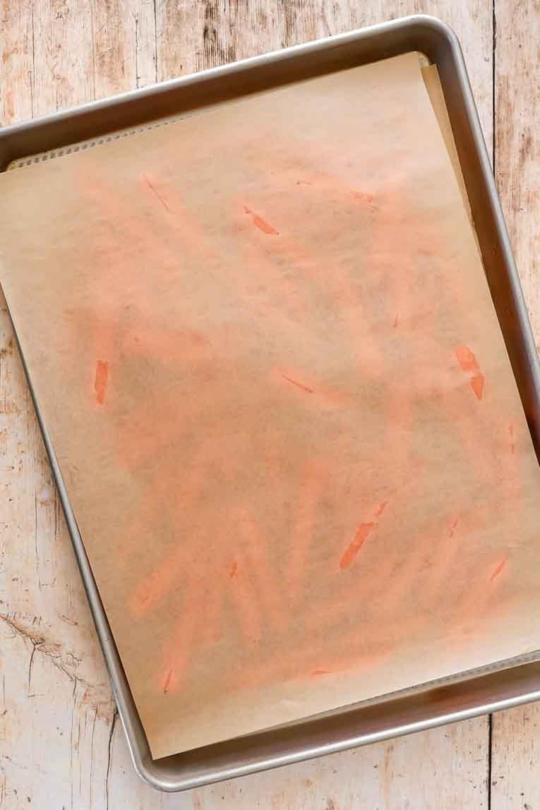 Carrots topped with parchment paper on a baking sheet.