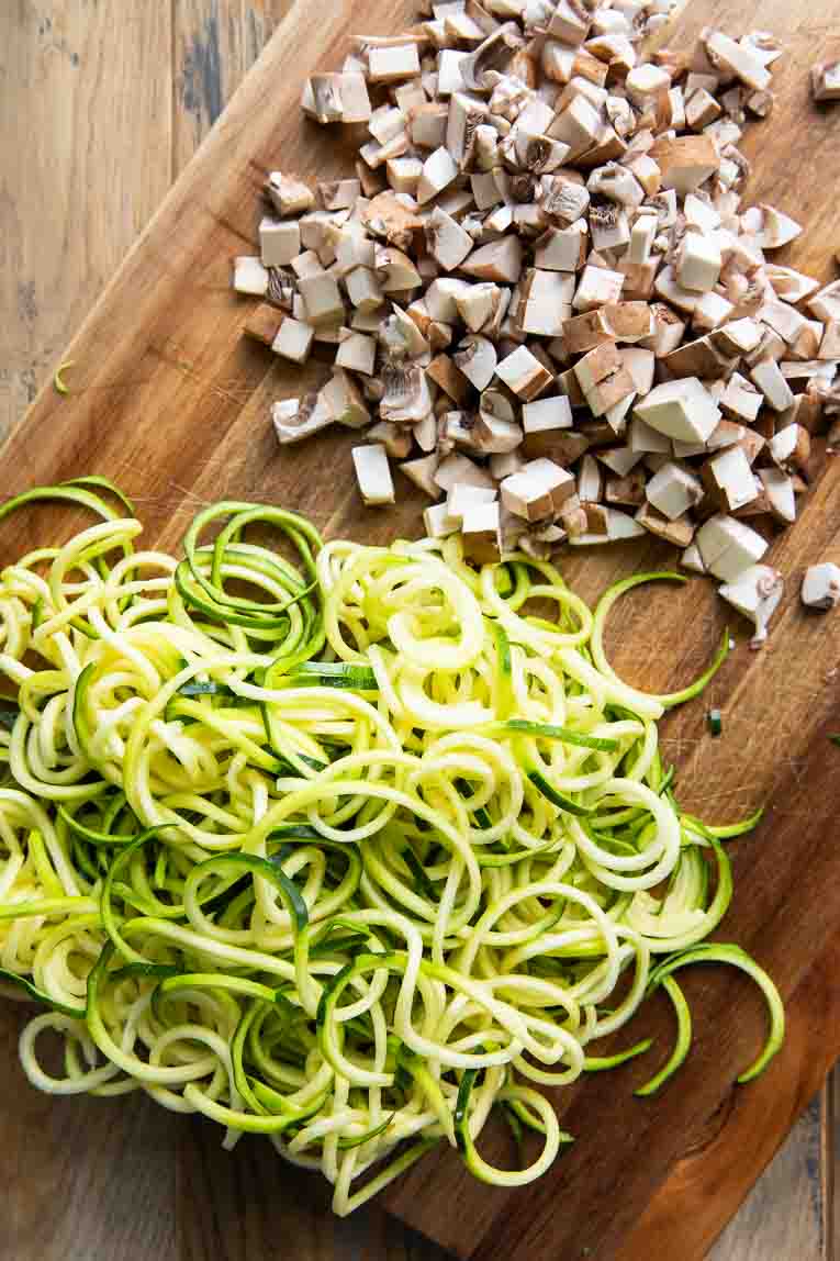 Spiralized Zucchini and chopped mushrooms on a cutting board.