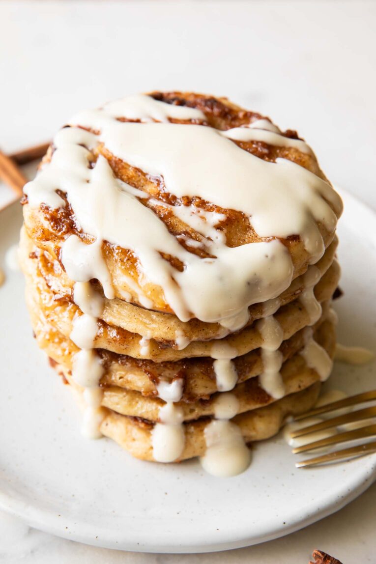 Angled view of a stack of cinnamon roll pancakes on a plate.