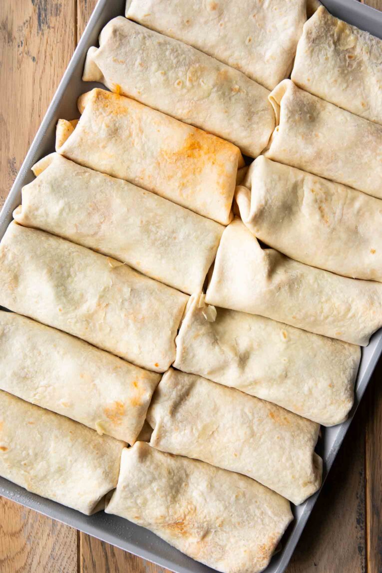 Burritos lined on a sheet pan.