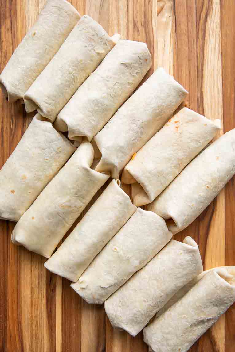 Burritos lined on a wooden surface.
