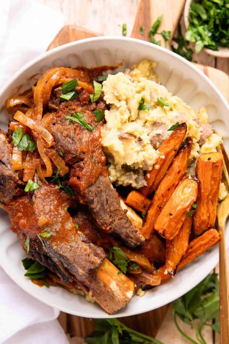 Slow cooker ribs on a plate with potatoes and veggies.