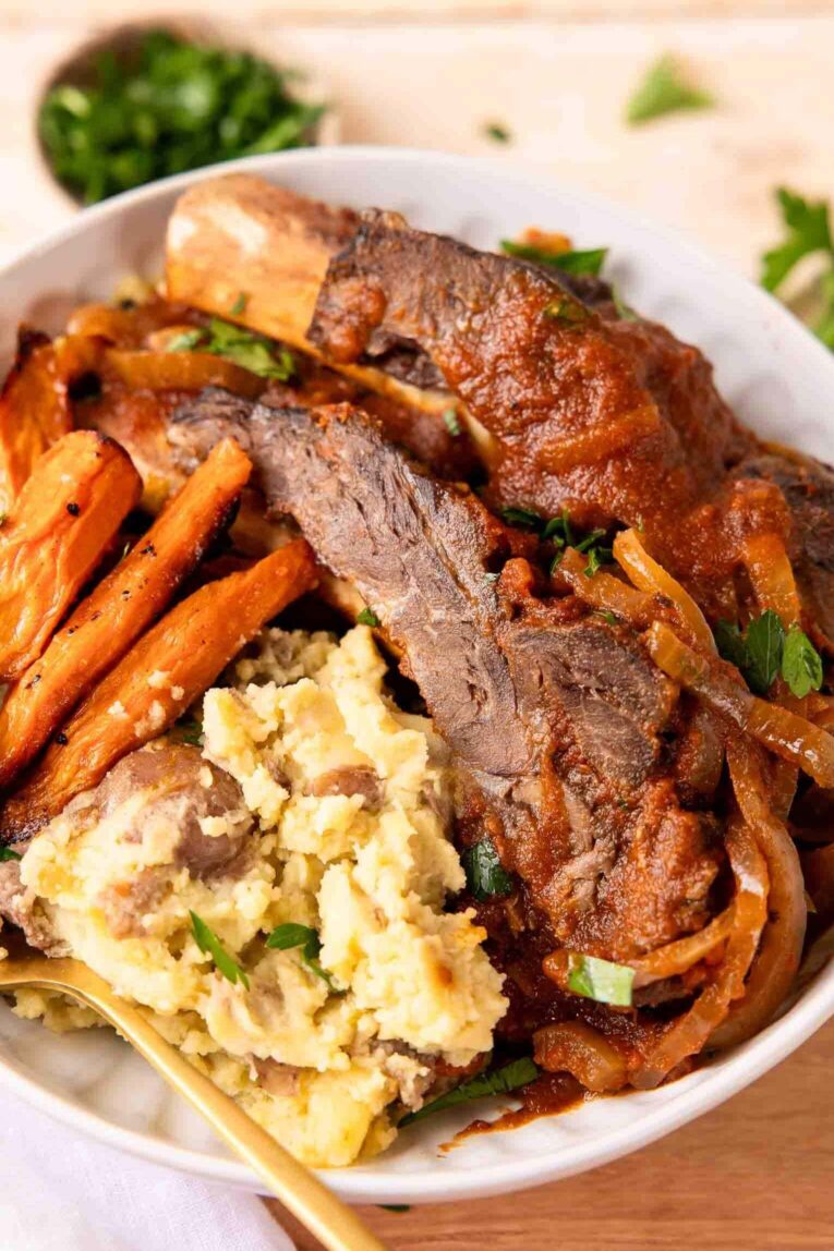 Slow cooker ribs on a plate with potatoes and veggies.