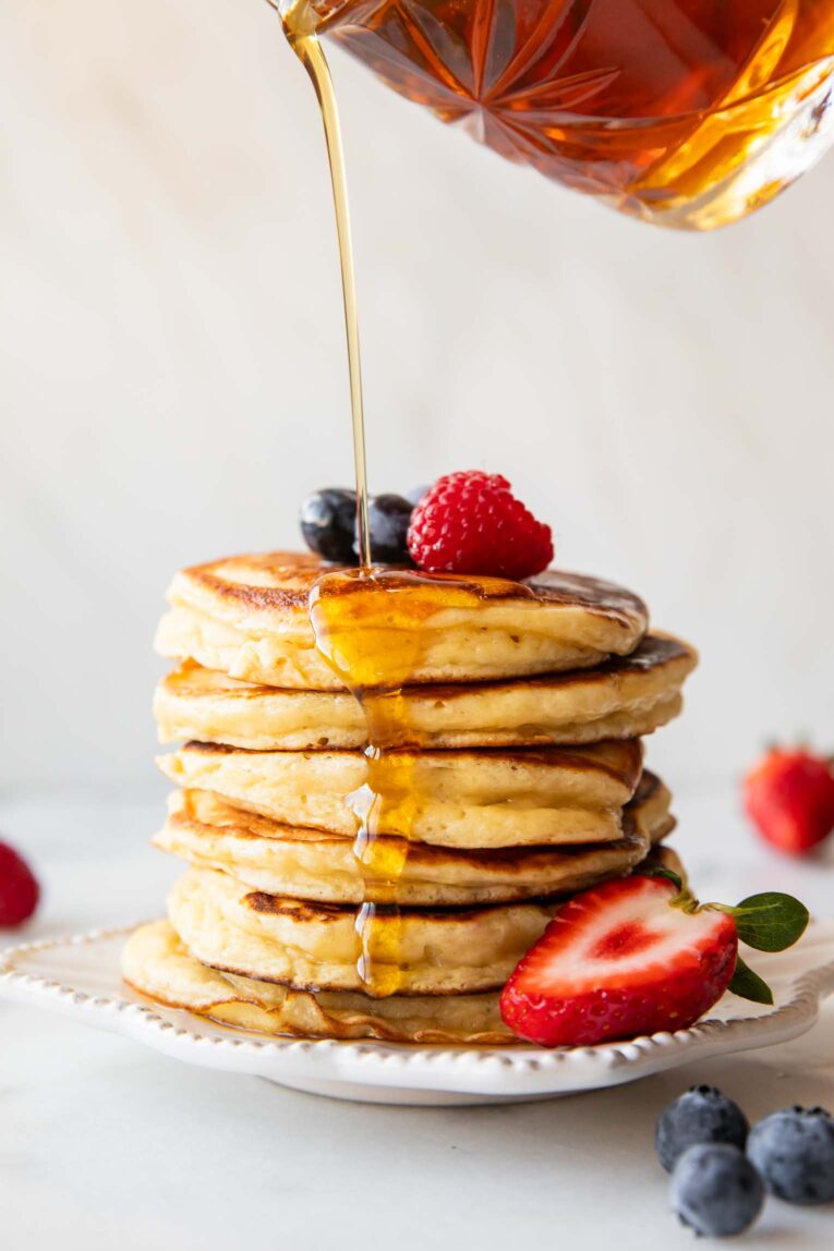 Maple Syrup being poured over a stack of greek yogurt pancakes.