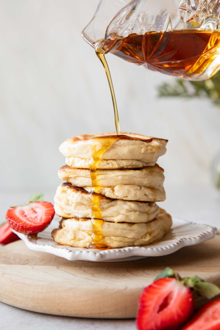 A stack of Souffle Pancakes on a plate with maple syrup being drizzled on top.