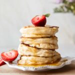 A stack of Souffle Pancakes on a plate topped with a strawberry.