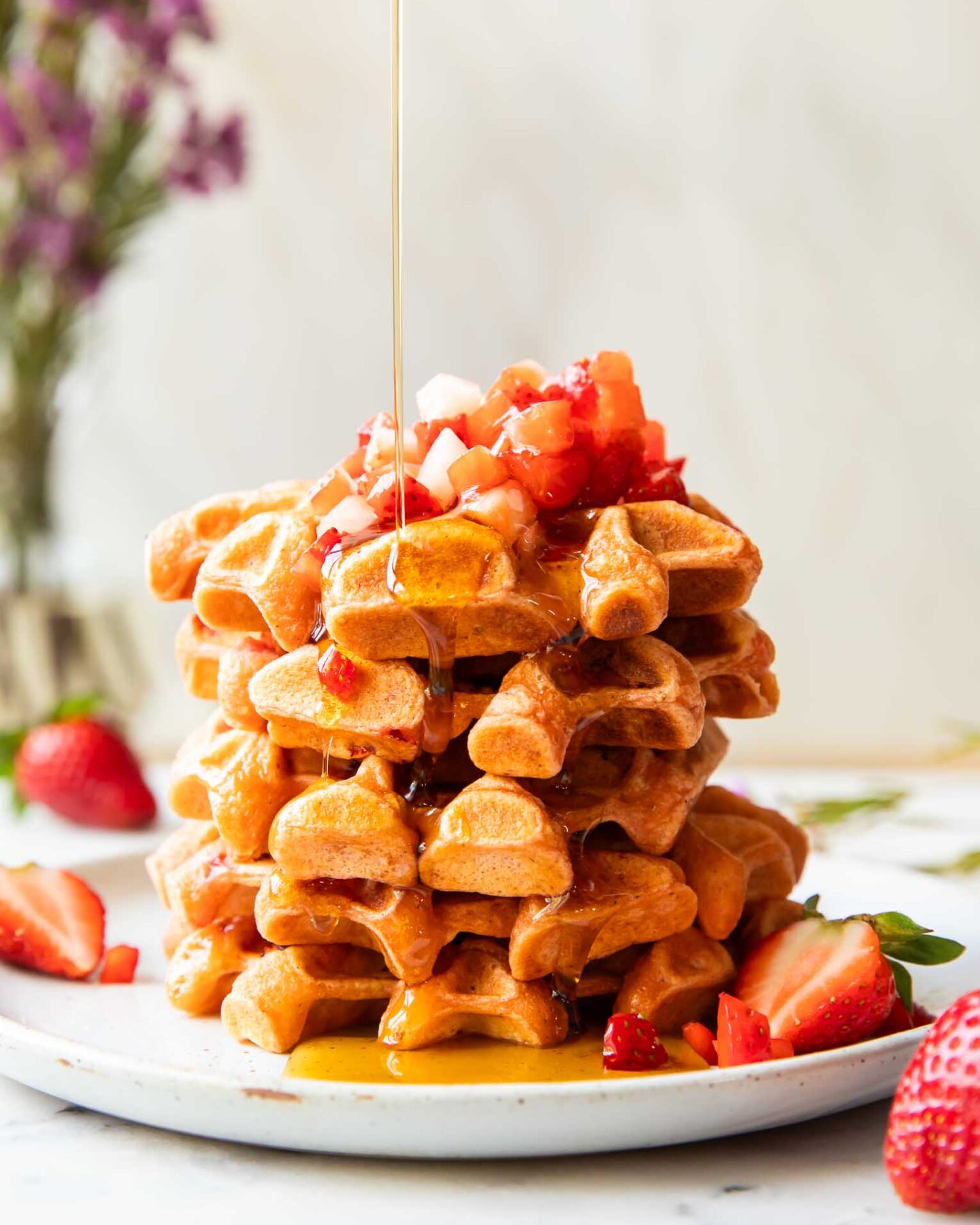 A stack of waffles on a plate with maple syrup.